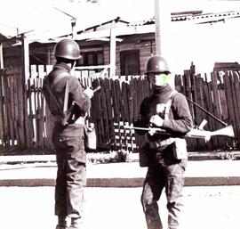 Dos Militares en tenida de combate vigilan una esquina de una población