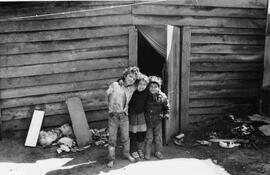 Tres niños muy sucios afuera de una casa de campamento abrazándose y sonriéndole a la cámara