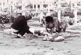 Dos personas en un cementerio, agachadas arreglando un tumba