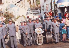 Militares con sus instrumentos musicales parados junto a civiles, en una calle