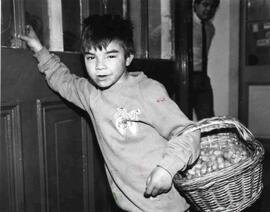 Niño chico entrando por una puerta, llevando una canasta con productos para venderlos