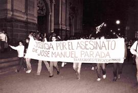 Manifestación pública nocturna en donde trabajadores llevan un lienzo que dice Justicia por el as...