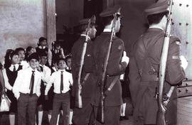 Niños en uniforme formados afuera del Palacio de la Moneda, mientras entran marchando tres carabi...