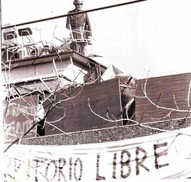 Carabinero subido a un techo, entre sillas puestas ahí, a causa de una manifestación